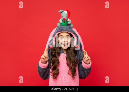 sorprendo il capretto nel pajama comodo tiene il giocattolo di natale su sfondo rosso, homewear Foto Stock