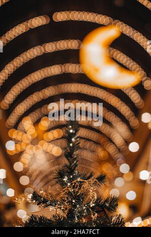 Albero di Natale magico decorato con giocattoli d'oro di Natale. Atmosfera festosa e decorazioni lucenti all'interno con luci bokeh garland e luna Foto Stock