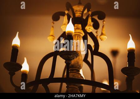 Su un vecchio ed elegante lampadario, le lampade a forma di candele emettono una luce luminosa e accogliente la sera. Un hotel o un palazzo. Elettricità. Foto Stock