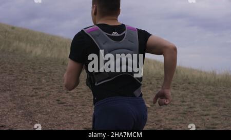 Caucasico maschio corridore corre su ripido sentiero polveroso in montagne secche. Atleta durante un intenso allenamento in montagna. L'uomo corre in salita. Foto Stock