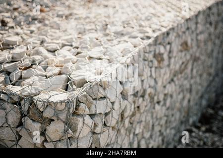 Pietre di granito dietro una griglia di metallo per rinforzare la pendenza. Pietre dietro il filo. Struttura grigia. Costruzione. Foto Stock