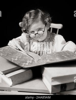 1930S RAGAZZA PICCOLA BRUNA CHE SORRIDE LEGGENDO USANDO UN GRANDE LIBRO DI RIFERIMENTO CHE INDOSSA GLI OCCHIALI CIRCOLARI STUDIOSO E GUARDANDO LA MACCHINA FOTOGRAFICA - J5098 HAR001 HARS HOME VITA COPIA SPAZIO CARATTERE FIDUCIA OCCHIALI B&W OCCHIO CONTATTO BRUNETTE SCUOLE SUCCESSO SOGNI GRADO TESTA DI RIFERIMENTO E SPALLE ALLEGRO SCOPERTA E CONOSCENZA INTELLIGENTE ORGOGLIO ACCADEMICO OPPORTUNITÀ OCCUPAZIONI SORRISI PRIMARI UTILIZZANDO GIOIOSO PIACEVOLE STUDIOSO INTELLIGENTE PIACEVOLE AFFASCINANTE SCUOLA DI GRADO CRESCITA GIOVANI LOVABLE PIACEVOLE STUDIOSO ADORABILE ATTRAENTE BIANCO E NERO ETNIA CAUCASICA HAR001 ANTIQUATO INQUISITIVO Foto Stock