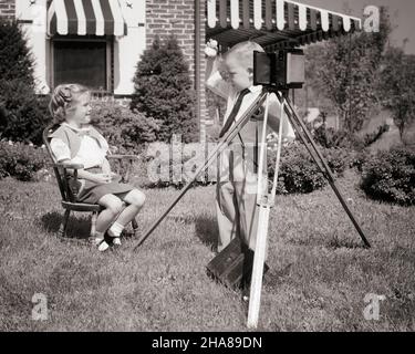 1950S RAGAZZA SEDUTA IN SEDIA IN IARDA IN POSA PER FOTOGRAFA RAGAZZO CHE INDOSSA LA CRAVATTA SCATTANDO LA SUA FOTO CON LA MACCHINA FOTOGRAFICA SUL TREPPIEDE - J5687 HAR001 HARS NOSTALGIA SPARARE VECCHIA MODA 1 FOTOGRAFIA CORTILE GIOVANILE FOTOGRAFO COMUNICAZIONE CARRIERA EQUILIBRIO LAVORO DI SQUADRA LIFESTYLE ATTORE FEMMINE LAVORI CASA VITA COPIA SPAZIO FULL-LENGTH PERSONE ISPIRAZIONE CURA MASCHI PROFESSIONE FIDUCIA AGIRE TREPPIEDE B&W VISIONE ABILITÀ OCCUPAZIONE FELICITÀ ABILITÀ PERFORMER CUSTOMER SERVICE CAREERS ENTUSIASMO TRAVAGLIO FOTOGRAFARE OPPORTUNITÀ AUTORITÀ IMPIEGO ENTERTAINER SCOLLIE OCCUPAZIONI POSANDO CONNESSIONE ATTORI CONCETTUALI Foto Stock