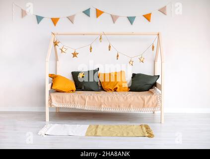 Elegante camera scandi per bambini con letto Montessori decorato con cuscini colorati, bandiere di carta e stelle dorate appese sulla corda per alzare il cheerfu Foto Stock