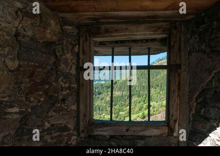 Vista attraverso una finestra barrata di un vecchio castello con un'ampia vista sul paesaggio montano Foto Stock