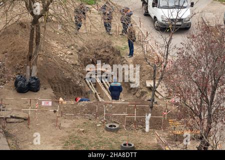 Tiraspol, Repubblica non riconosciuta di Transnistria - 18 novembre 2021: Un gruppo di lavoratori svolge lavori di riparazione su una rete di riscaldamento in una a residenziale Foto Stock