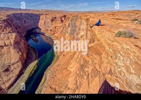 Un uomo seduto sul bordo di una scogliera che domina Horseshoe Bend vicino a Page Arizona. Foto Stock