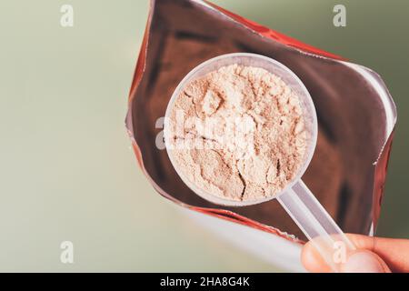 Cucchiaio per la misurazione delle proteine del siero di latte in primo piano sul sacchetto aperto su sfondo verde, vista dall'alto Foto Stock