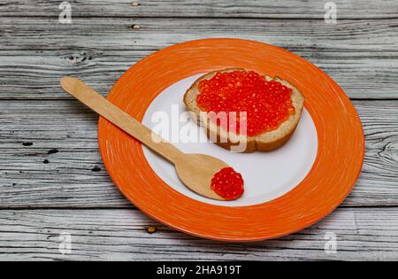 sandwich con caviale rosso adagiato su un piatto arancione su sfondo di legno. Foto di alta qualità Foto Stock