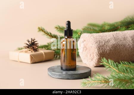 Concetto di Spa di Natale con olio cosmetico aromatico, rami sempreverdi su sfondo beige. Cura del corpo invernale, armonia e benessere. Primo piano. Foto Stock