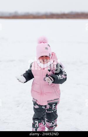 Bambina su strada innevata d'inverno. Il bambino in tuta rosa d'inverno corre attraverso la neve sullo sfondo della foresta invernale Foto Stock