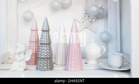 Figurine in ceramica di alberi di Natale color pastello, un angelo di fedi bianco, una ghirlanda di palle fatte di fili decorano la stanza prima di Natale Foto Stock