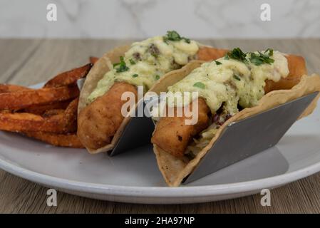 Presentazione artistica di tacos di pesce fritto croccante ricoperti di formaggio fuso e serviti con patatine fritte croccanti. Foto Stock