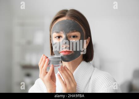 Giovane donna con maschera di carbone attiva sul suo volto a casa Foto Stock