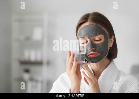 Giovane donna con maschera di carbone attiva sul suo volto a casa Foto Stock