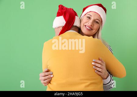 Coppia matura hugging in Babbo Natale cappelli su sfondo a colori Foto Stock