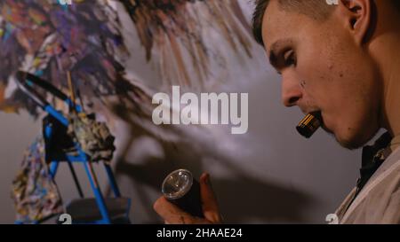 Artista designer disegna un aquila sulla parete. Artigiano arredatore dipinge un quadro con olio acrilico colore. Fumi Vaper vape. Pittore pittore vestito in Foto Stock
