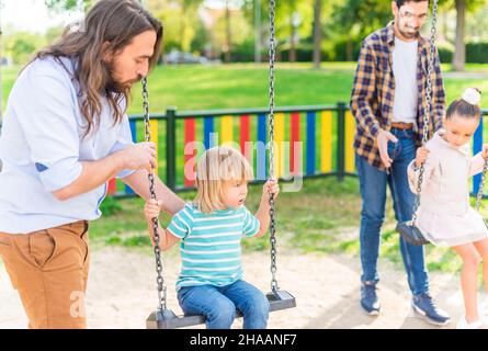 Una giovane coppia gay che gioca con i propri figli in altalena Foto Stock