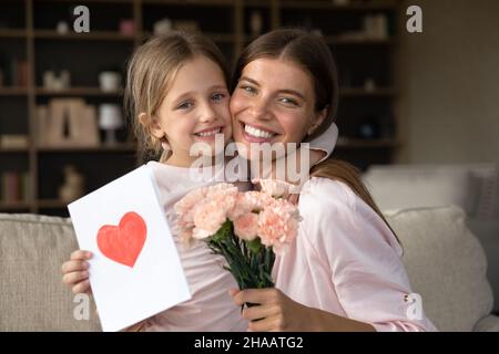 Mamma grata che abbraccia la figlia ragazza, che tiene bouquet di fiori Foto Stock