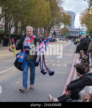 Un uomo cammina lungo Victoria Embankment vendendo striscioni inglesi e bandiere britanniche prima del Lord Mayor’s Show, 2021. Walkie Talkie in background. Foto Stock