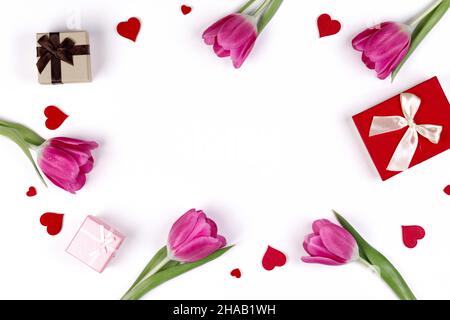 Cornice da giorno piatta con cuori di tulipani rosa e scatole regalo su sfondo bianco Foto Stock