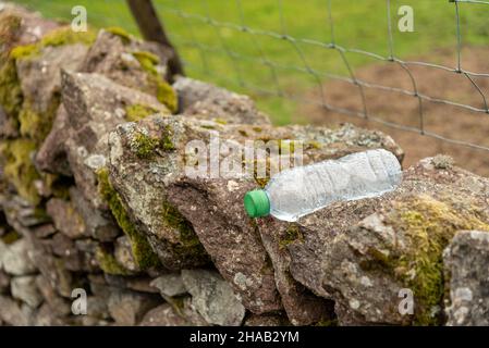 svuotare la bottiglia dell'acqua scartata su una parete di pietra asciutta, problema ambientale Foto Stock