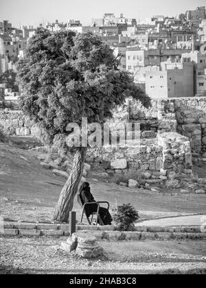 Donna araba su una panca nella Cittadella di Amman che indossa un abito nero tradizionale abaya Foto Stock