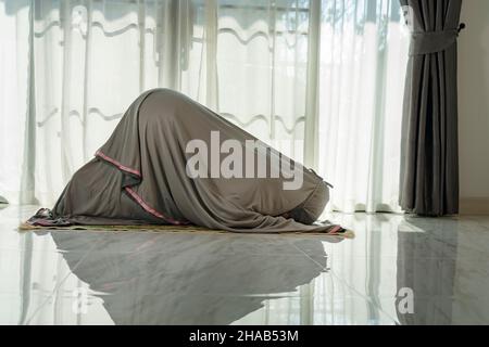 Donna musulmana che prega in salotto a casa. Diario di dovere di religione. Silhouette di persone Foto Stock