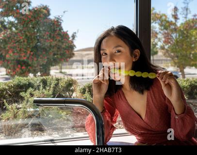 donna che mangia uno spiedino di uva in una cucina con grandi finestre, strada sullo sfondo Foto Stock