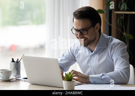L'uomo d'affari si siede alla scrivania guardando lo schermo del laptop si sente soddisfatto Foto Stock
