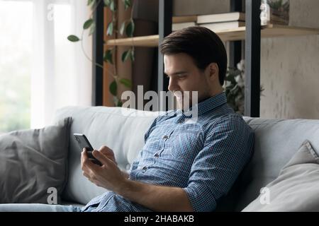 Il giovane si siede sul divano con smartphone Foto Stock