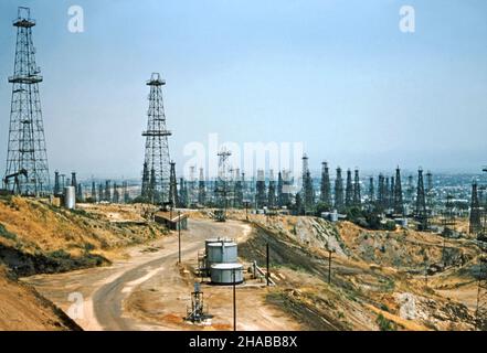 Oilwells a Signal Hill, Long Beach, California, USA nel giugno 1954 – questa vista mostra quanto vicino il campo petrolifero è urbano Los Angeles e l'Oceano Pacifico oltre. Si possono vedere derrick in legno e acciaio, oltre a uno o due “asini annuenti” (pompjack) e serbatoi di stoccaggio. Il Long Beach Oil Field è stato scoperto nel 1921. Il periodo di massimo splendore del campo è stato il 1920s, con centinaia di derrick petroliferi che coprono Signal Hill e le parti adiacenti di Long Beach. Il campo è ormai in gran parte esaurito – una fotografia d'epoca del 1950s. Foto Stock