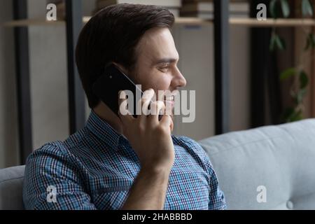 Uomo seduto sul divano in soggiorno che parla sul cellulare Foto Stock