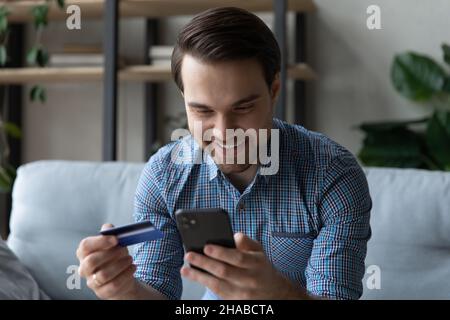 L'uomo sorridente tiene lo smartphone utilizzando la carta di credito che acquista merci online Foto Stock