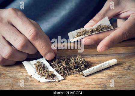 Sfuso tabacco arrotolabile con le mani di un uomo che arrotola una sigaretta sullo sfondo Foto Stock