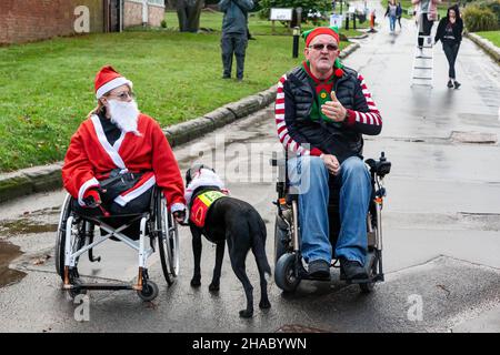 Warrington, Regno Unito. Domenica 12 Dicembre 2021 - ThisAbility2021 - Walton Hall and Gardens. Dopo una pausa di un anno, l'annuale Santa Dash/Santa Walk 3K organizzato dalla Warrington Disability Partnership anche se il tempo pioveva all'inizio. Dave Thompson MBE DL MBA dà un discorso introduttivo ai corridori mentre una donna senza gambe, Jill Keast Doran, siede da lui Credit: John Hopkins/Alamy Live News Foto Stock