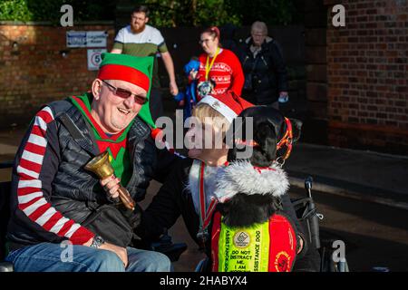 Warrington, Regno Unito. Domenica 12 Dicembre 2021 - Walton Hall and Gardens. Dopo una pausa di un anno, l'annuale Santa Dash/Santa Walk 3K organizzato dalla Warrington Disability Partnership anche se il tempo pioveva all'inizio. Dave Thompson MBE DL MBA si congratula con la signora, Jill Keast Doran, che ha completato 0,75K senza gambe come il suo cane di assistenza si unisce alle celebrazioni Credit: John Hopkins/Alamy Live News Foto Stock