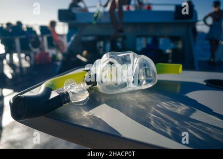 maschera e attrezzatura subacquea su tavola in legno nel mare dei caraibi con barca sullo sfondo. Foto di alta qualità Foto Stock