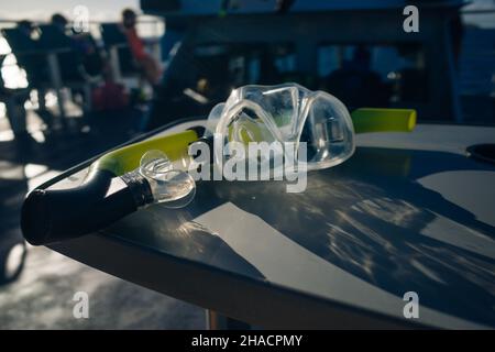 maschera e attrezzatura subacquea su tavola in legno nel mare dei caraibi con barca sullo sfondo. Foto di alta qualità Foto Stock