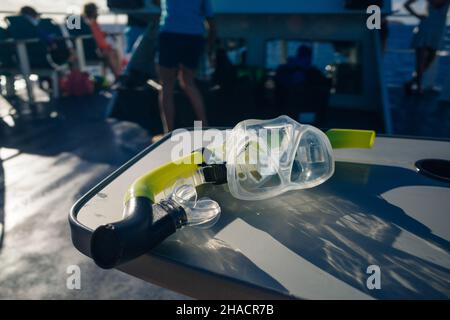 maschera e attrezzatura subacquea su tavola in legno nel mare dei caraibi con barca sullo sfondo. Foto di alta qualità Foto Stock