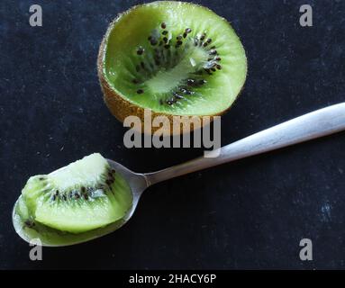 Fotografia di kiwi mangiato e cucchiaio su sfondo ardesia per illustrazione del cibo Foto Stock