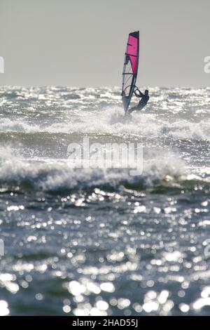 Windsurf vela Equitazione onde su Un mare agitato in Christchurch Bay UK Foto Stock