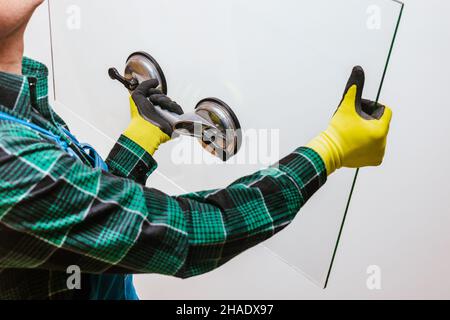 Glazier che tiene nelle mani un pezzo di vetro spesso con l'aiuto di una speciale ventosa, sfondo chiaro Foto Stock