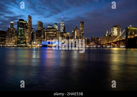 Parte dello skyline di Lower Manhattan e del ponte di Brooklyn sono sparati subito dopo il tramonto con dettagli nel cielo e grattacieli ligthed in contrasto con esso. Foto Stock