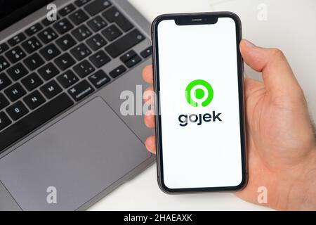 Piattaforma finanziaria Gojek per il trasferimento di denaro tramite smartphone. Mano uomo che tiene un telefono cellulare con l'applicazione sullo schermo e notebook sullo sfondo. Novembre 2021, San Francisco, USA Foto Stock