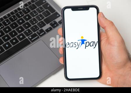 Piattaforma finanziaria Easy Pay per il trasferimento di denaro tramite smartphone. Mano uomo che tiene un telefono cellulare con l'applicazione sullo schermo e notebook sullo sfondo. Novembre 2021, San Francisco, USA Foto Stock