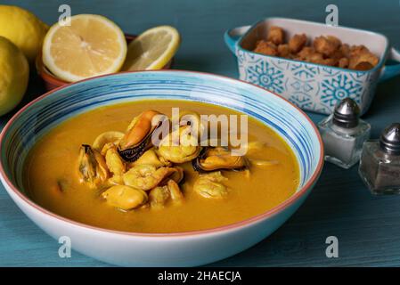 Zuppa di pesce a base di gamberi, cozze, vongole, naselli e calamari, servito con pane fritto e limoni. Foto Stock
