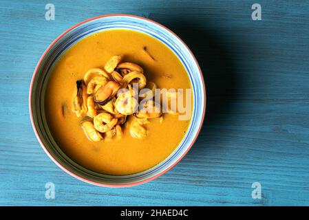 Zuppa di pesce a base di gamberi, cozze, vongole, naselli e calamari, servito con pane fritto e limoni, su un tavolo di legno scuro. Foto Stock
