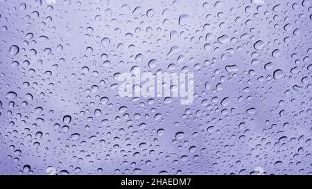 Colore dell'anno 2022 molto Peri. Parabrezza bagnato, preso dall'interno della macchina.la pioggia cade sulla superficie di una finestra di vetro della macchina con uno sfondo grigio Foto Stock