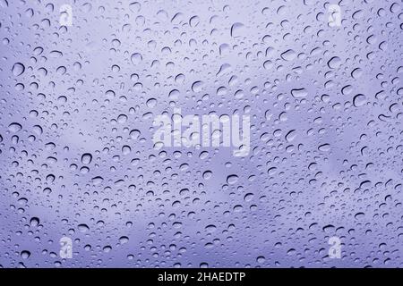 Colore dell'anno 2022 molto Peri. Parabrezza bagnato, preso dall'interno della macchina.la pioggia cade sulla superficie di una finestra di vetro della macchina con uno sfondo grigio Foto Stock